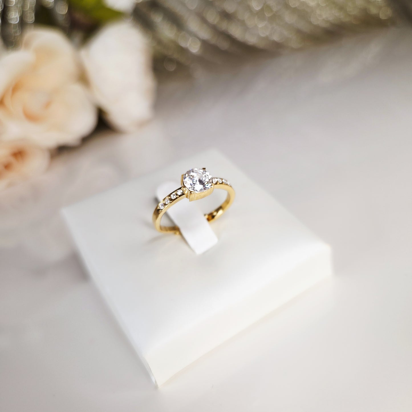 Bague dorée femme en acier inoxydable avec zircon rond central et incrustations de pierres scintillantes, bijou élégant et raffiné idéal pour mariage, fiançailles ou cadeau. Sur présentoir
