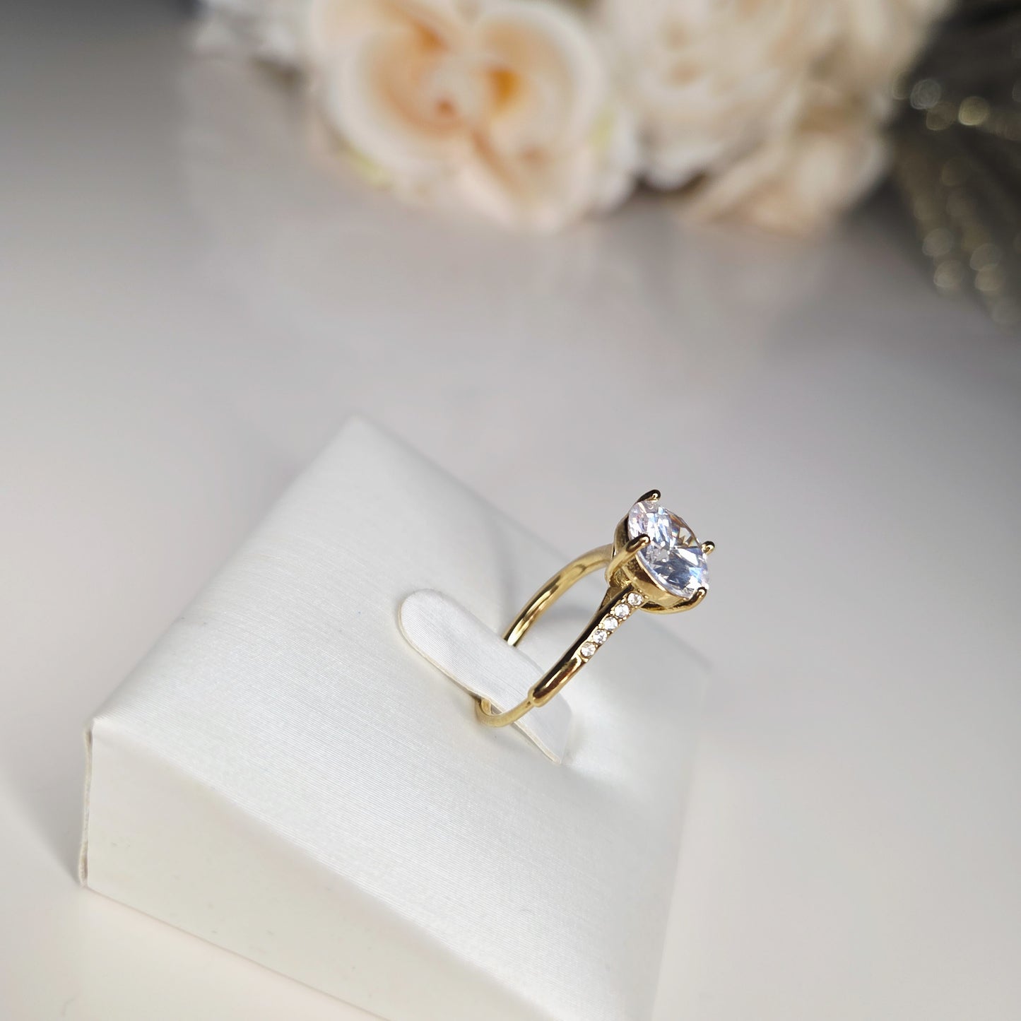Sublimez vos mains avec cette bague solitaire dorée, mise en valeur par une pierre ronde étincelante. Vue de côté.