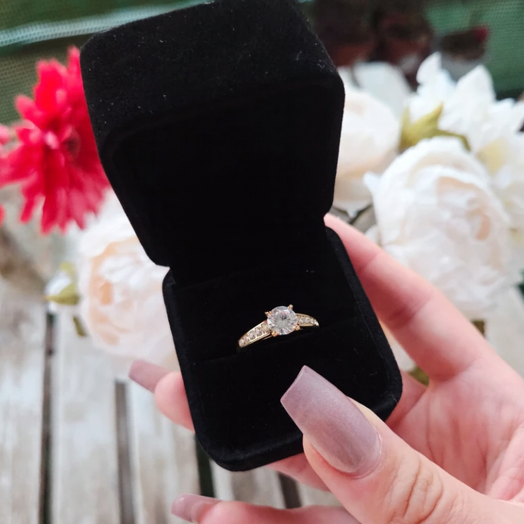 Bague solitaire en acier inoxydable doré avec un zircon rond et des pavés latéraux, présentée dans un coffret en velours noir