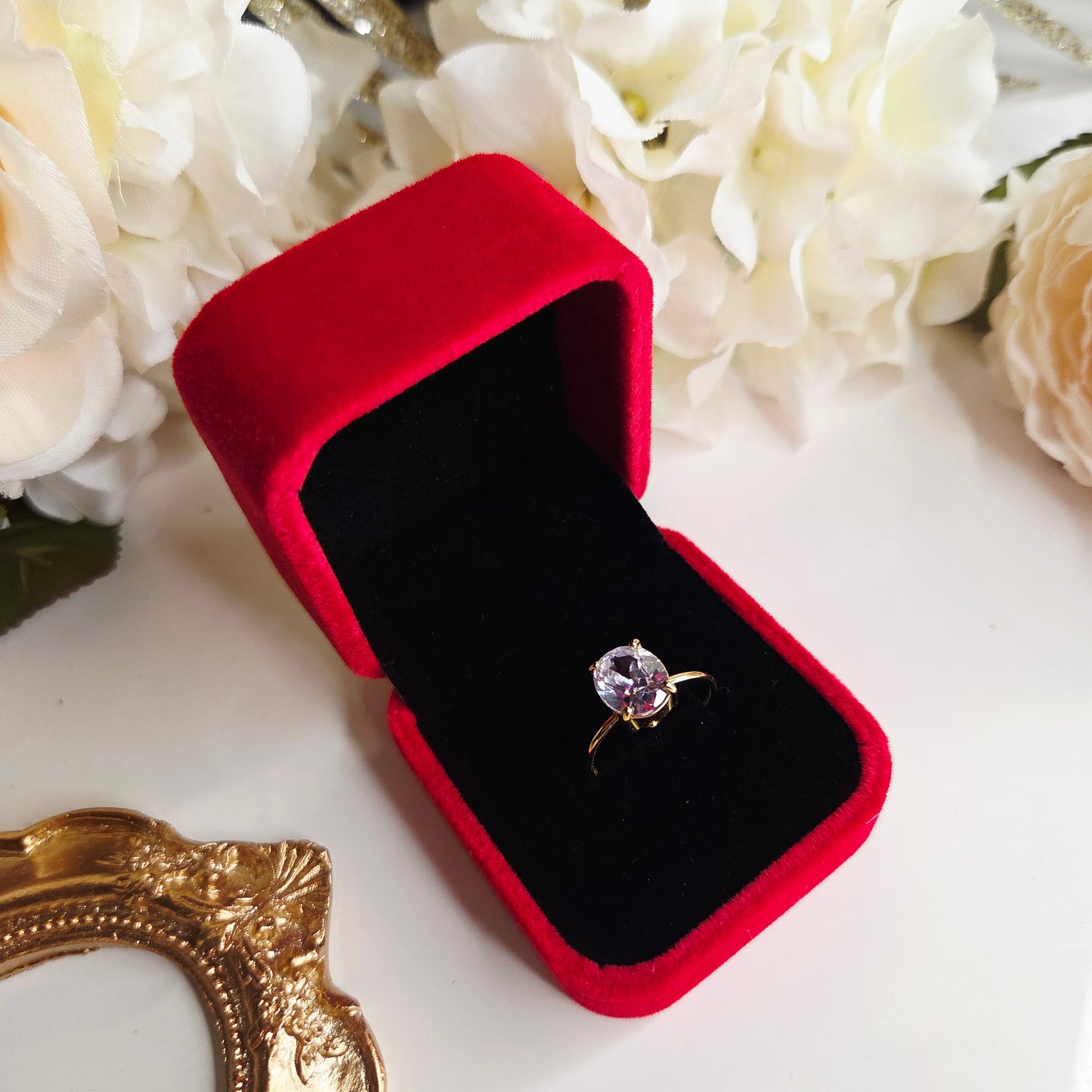 Bague solitaire dorée avec pierre ronde dans un écrin rouge velours ouvert