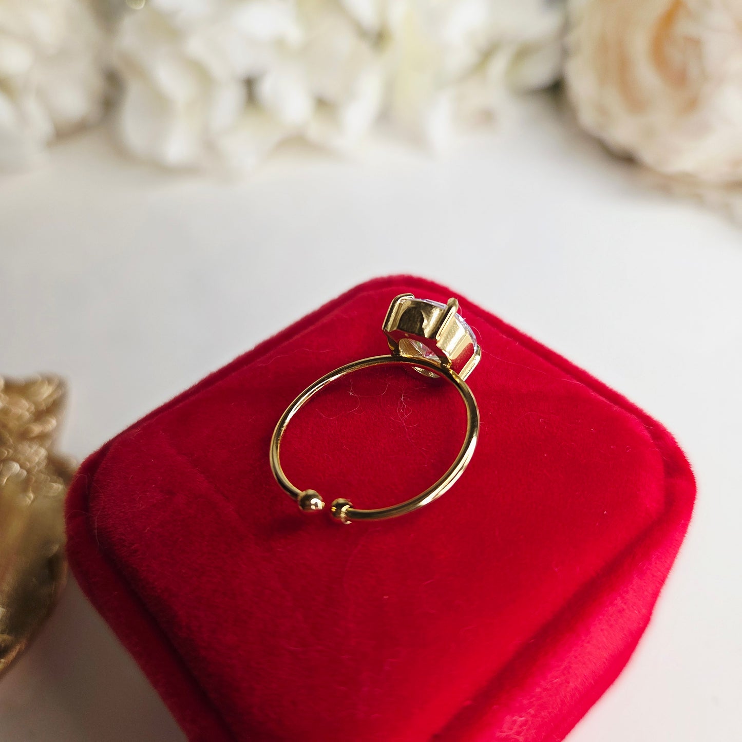 Bague solitaire dorée pour femme, sertie d’une pierre ronde brillante effet diamant, présentée dans un écrin rouge luxueux, bijou idéal pour offrir.