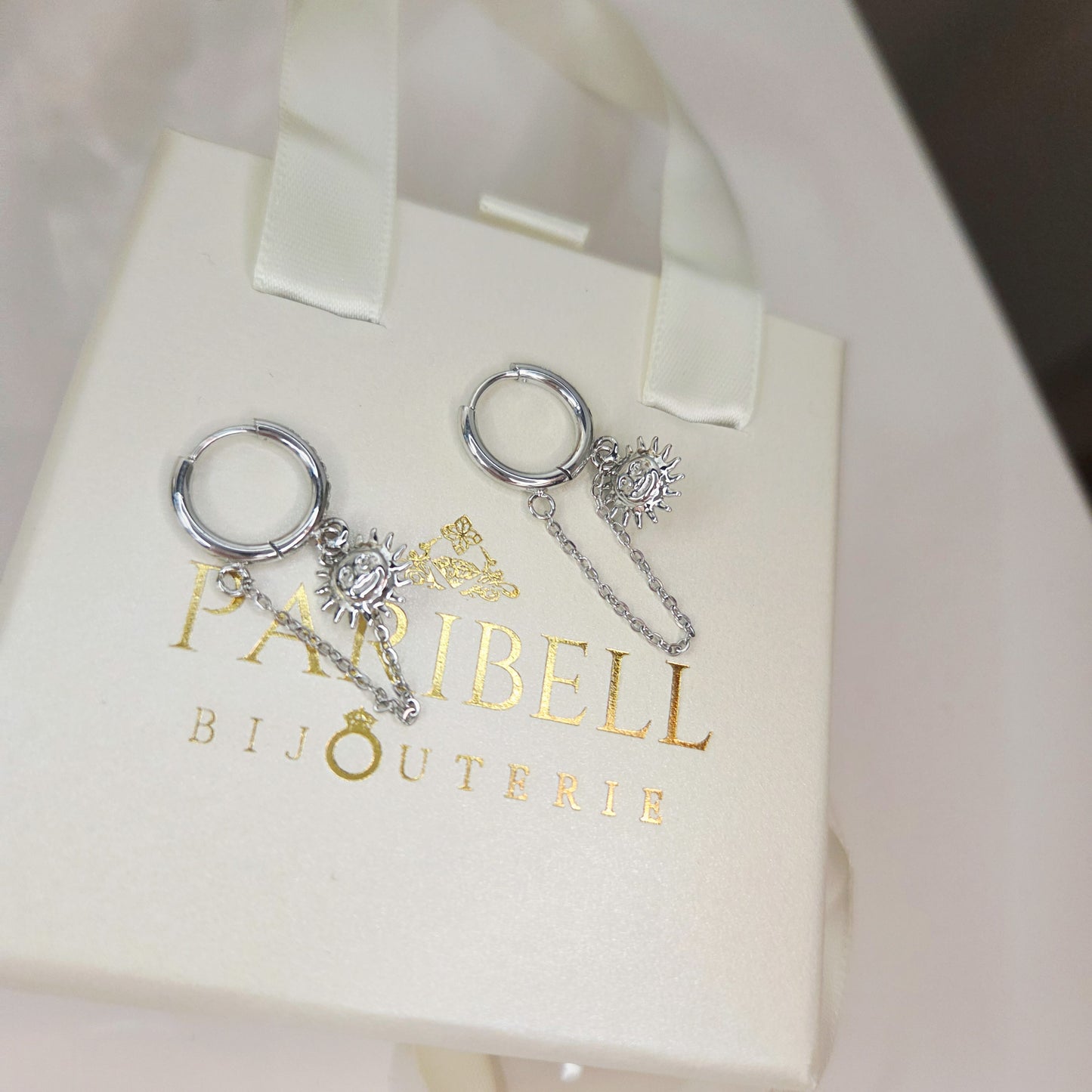 Paire de boucles d’oreilles anneaux avec chaînes pendantes et breloque soleil. Bijou élégant et féminin, facile à porter au quotidien.