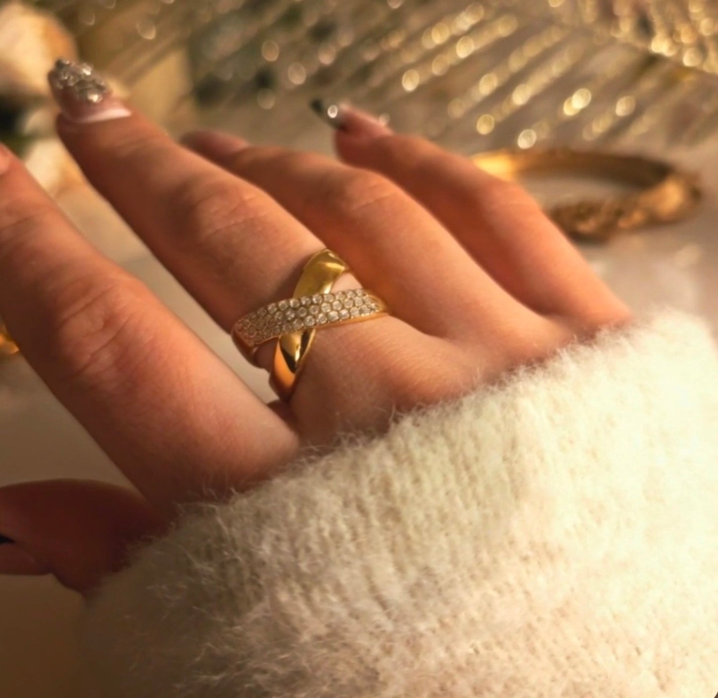 Bague dorée croisée avec bande pavée de pierres blanches portée à la main