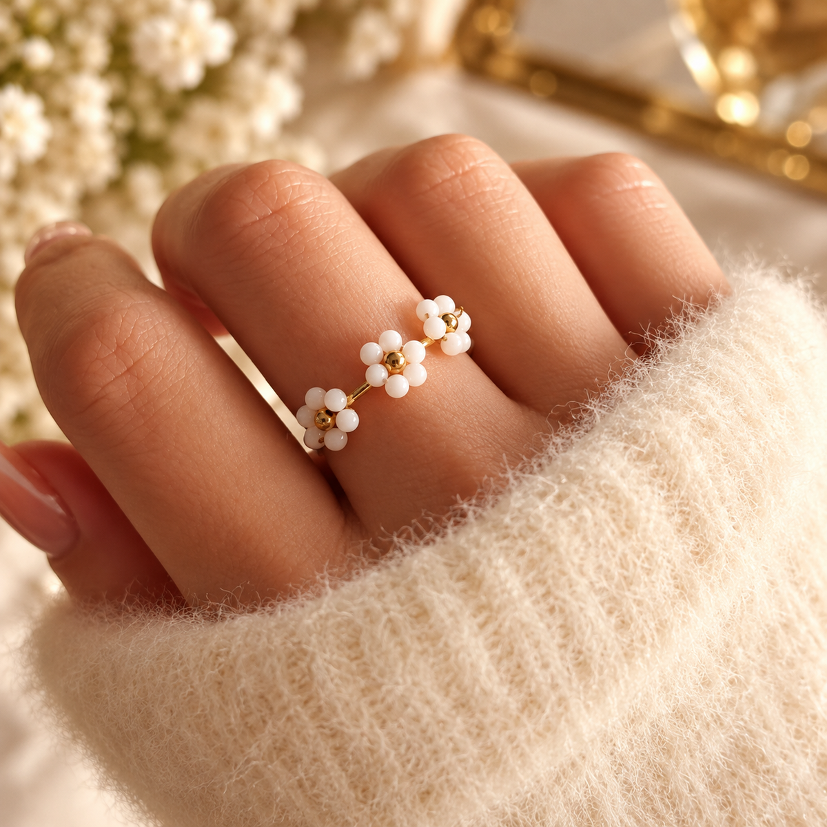 Bague dorée à trois petites fleurs de perles blanches et centres dorés, portée à la main