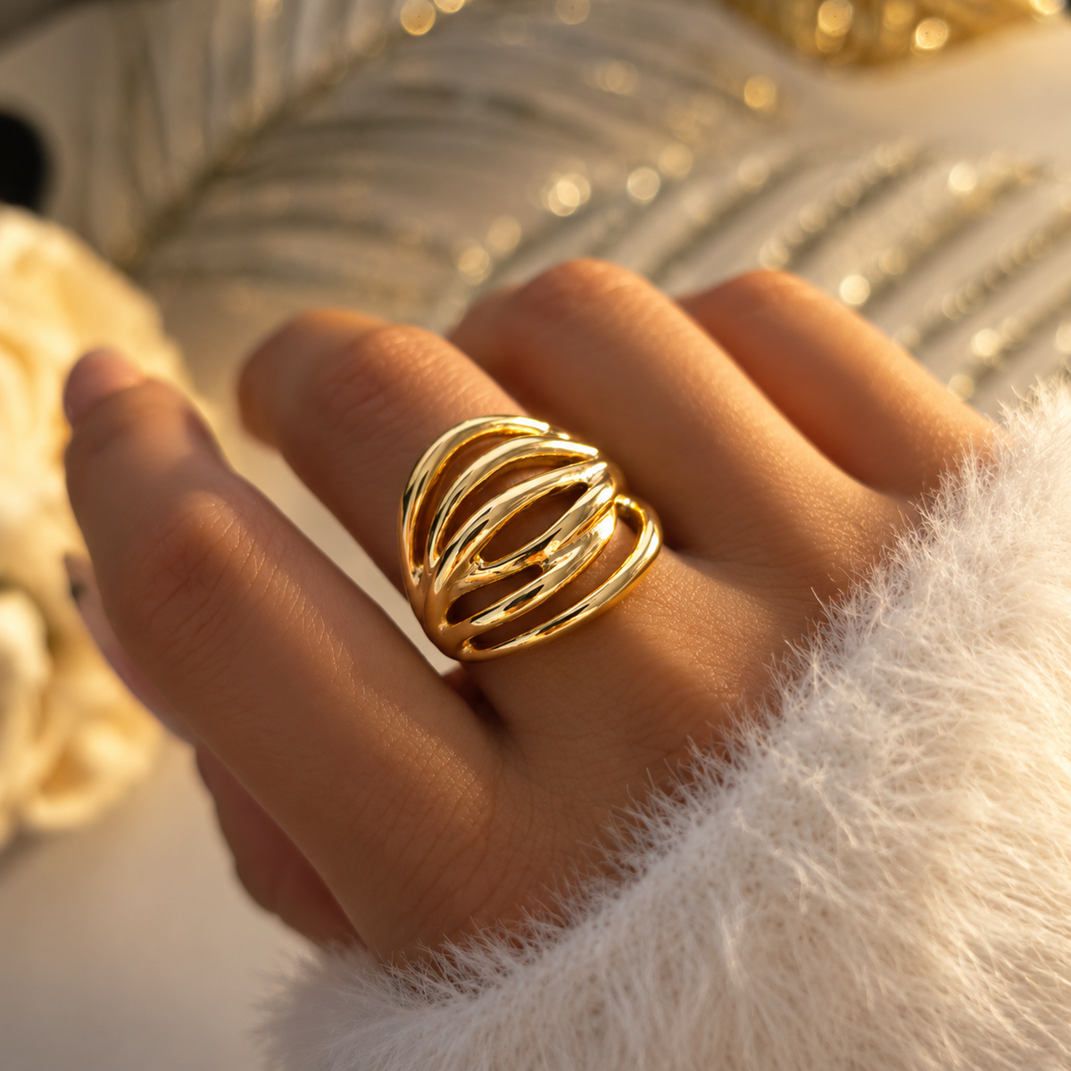 Bague large dorée à lignes courbes et ouvertures ovales, portée à la main