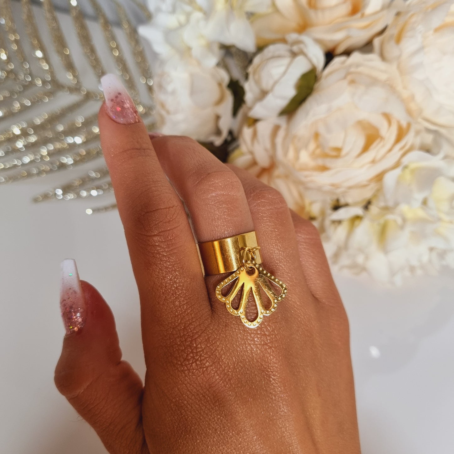 Bague réglable en acier doré, ornée d’un pendentif ajouré en forme d’éventail, portée sur une main féminine. Création artisanale fabriquée à la main dans le sud de la France. Idéale comme cadeau unique pour une femme élégante, cette bague évoque le charme, l’originalité et la délicatesse d’un bijou fait avec passion.