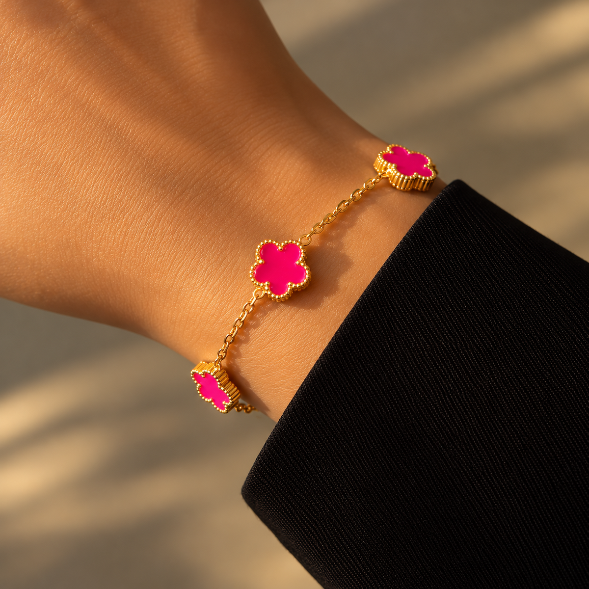 Bracelet à chaîne dorée et motifs trèfles rose fuchsia à contours perlés, porté au poignet