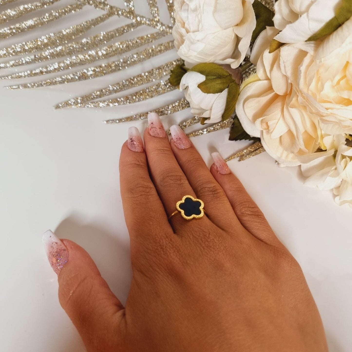 Photo portée d'une jolie bague dorée en acier inoxydable, ornée d'une pierre noire lisse et brillante sous forme de fleur ou trèfle à 5 feuilles. Taille réglable.