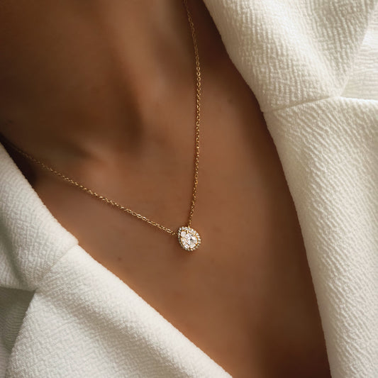 Collier pendentif goutte sertie porté au cou sur une chaîne fine