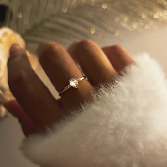 Bague dorée avec pierre en forme de goutte brillante portée au doigt