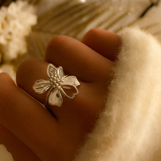 Bague ajustable en acier inoxydable argenté avec une grande fleur ajourée et un cœur perlé, portée sur une main