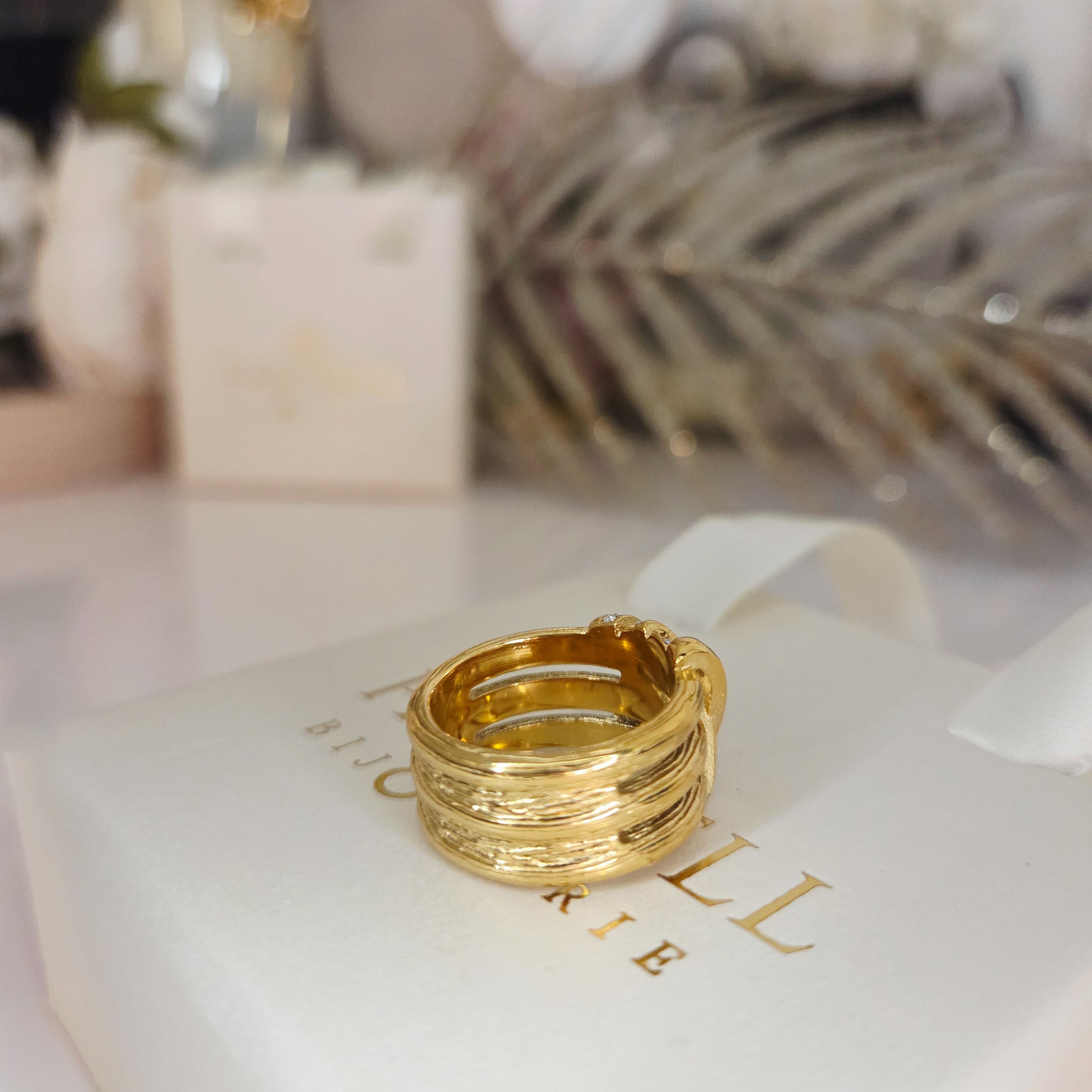 Bague large dorée avec texture travaillée et strass scintillants. Bijou chic et élégant, effet couture.