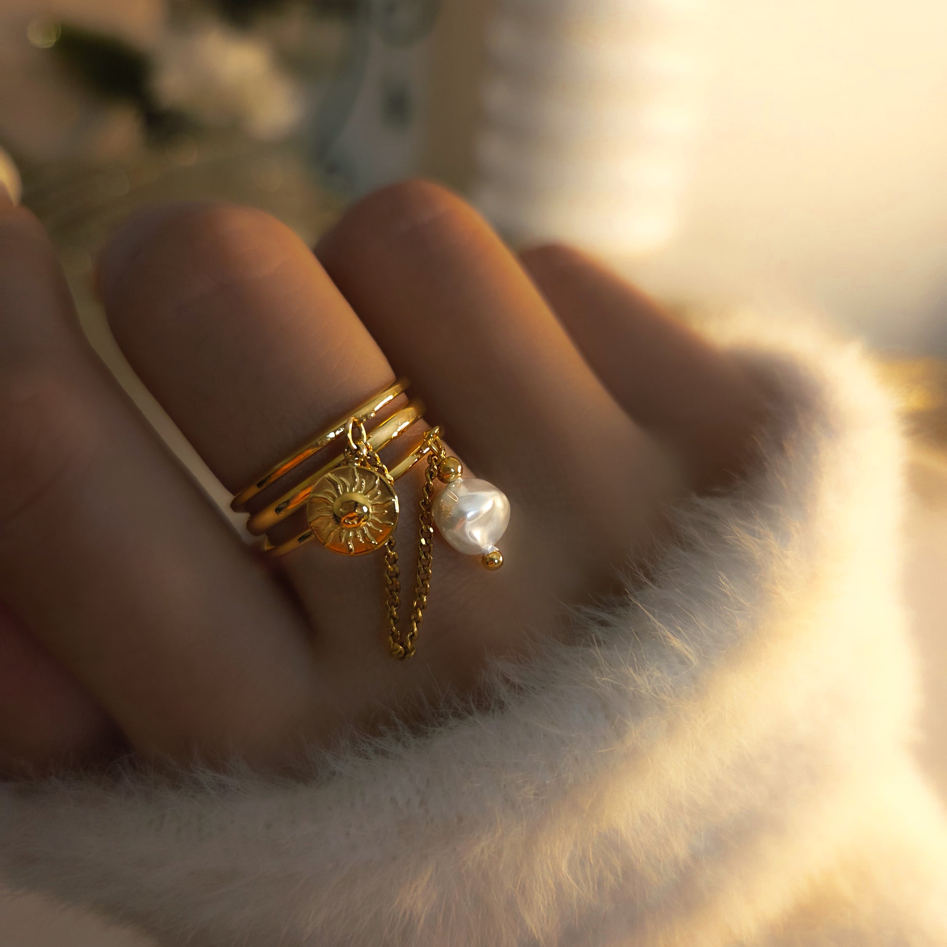 Bague multi-anneaux dorée avec pendentif soleil, perle et chaîne fine portée à la main