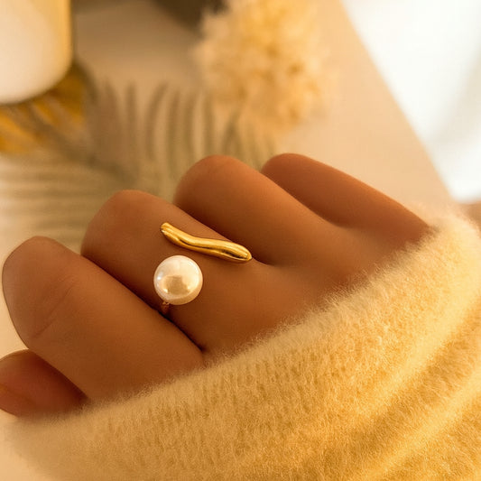 Bague ouverte en acier doré avec une perle nacrée et une barre organique, portée sur une main