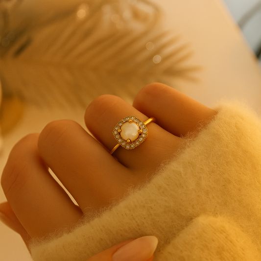 Bague en acier inoxydable doré avec perle centrale nacrée entourée de zircons étincelants, portée sur une main