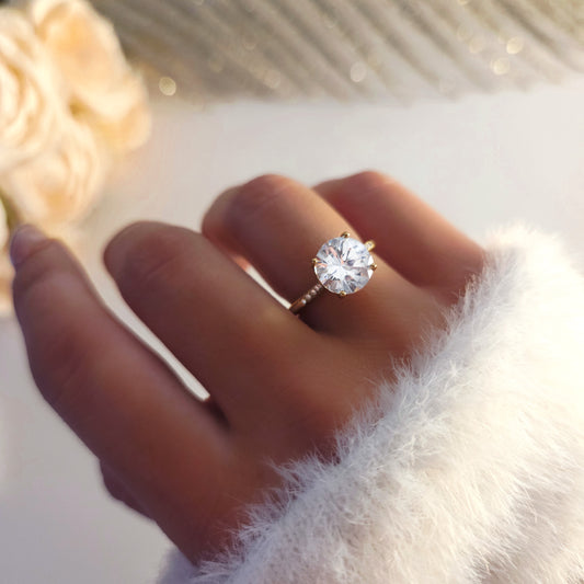 Bague solitaire dorée avec pierre ronde brillante portée au doigt zoom sur la pierre