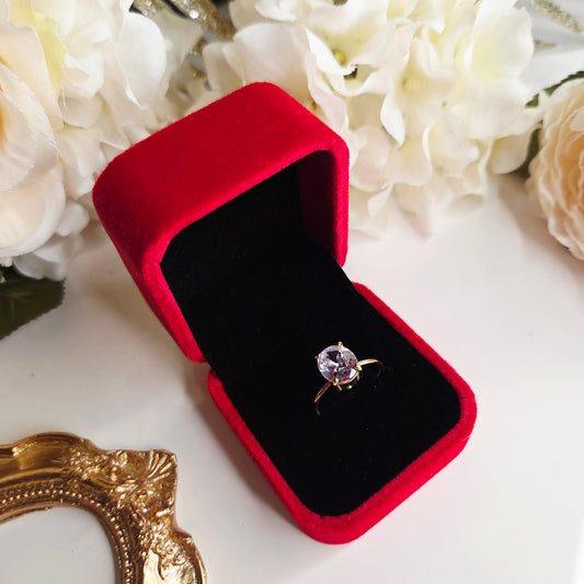 Bague solitaire dorée avec pierre ronde dans un écrin rouge velours ouvert