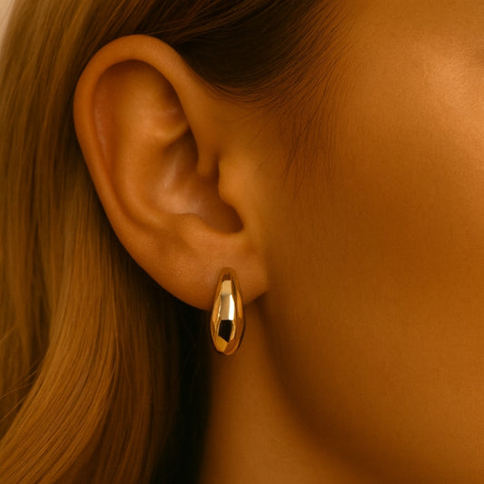 Photo portée de boucles d'oreilles créoles relief géométrique, couleur dorée, en forme de banane. 