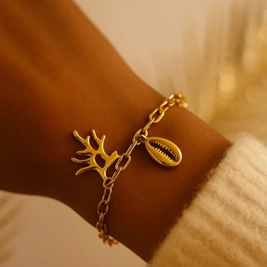 Bracelet en acier inoxydable doré avec pendentif corail et coquillage cauri, porté au poignet