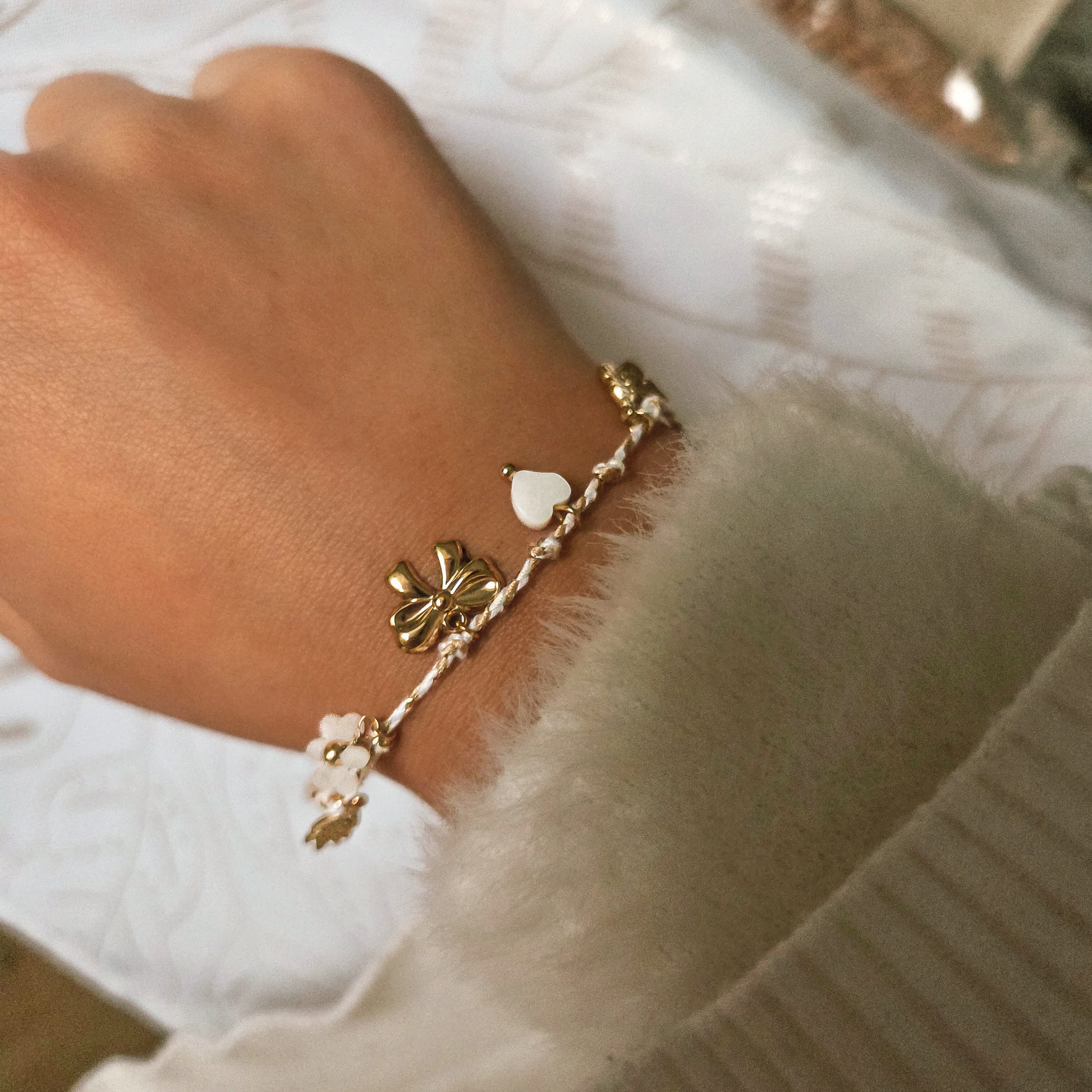 Bracelet cordon blanc avec charms dorés et perles porté au poignet, bijou délicat et féminin