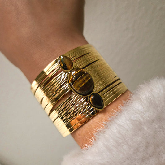 Manchette large dorée avec pierres effet œil de tigre portée au poignet, bijou audacieux et élégant