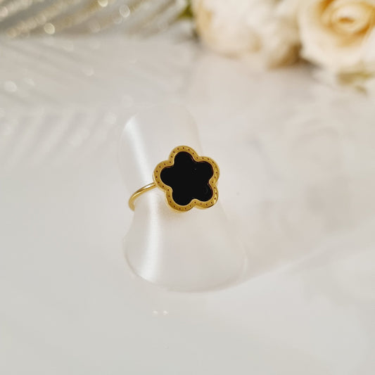 Bague dorée et noire sur présentoir, ornée d'une fleur noire en pierre lisse. Taille réglable.