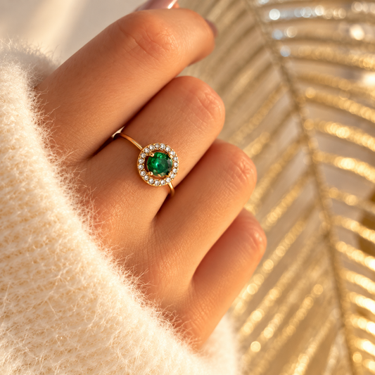 Bague dorée à pierre ronde verte entourée de petites pierres transparentes, portée à la main