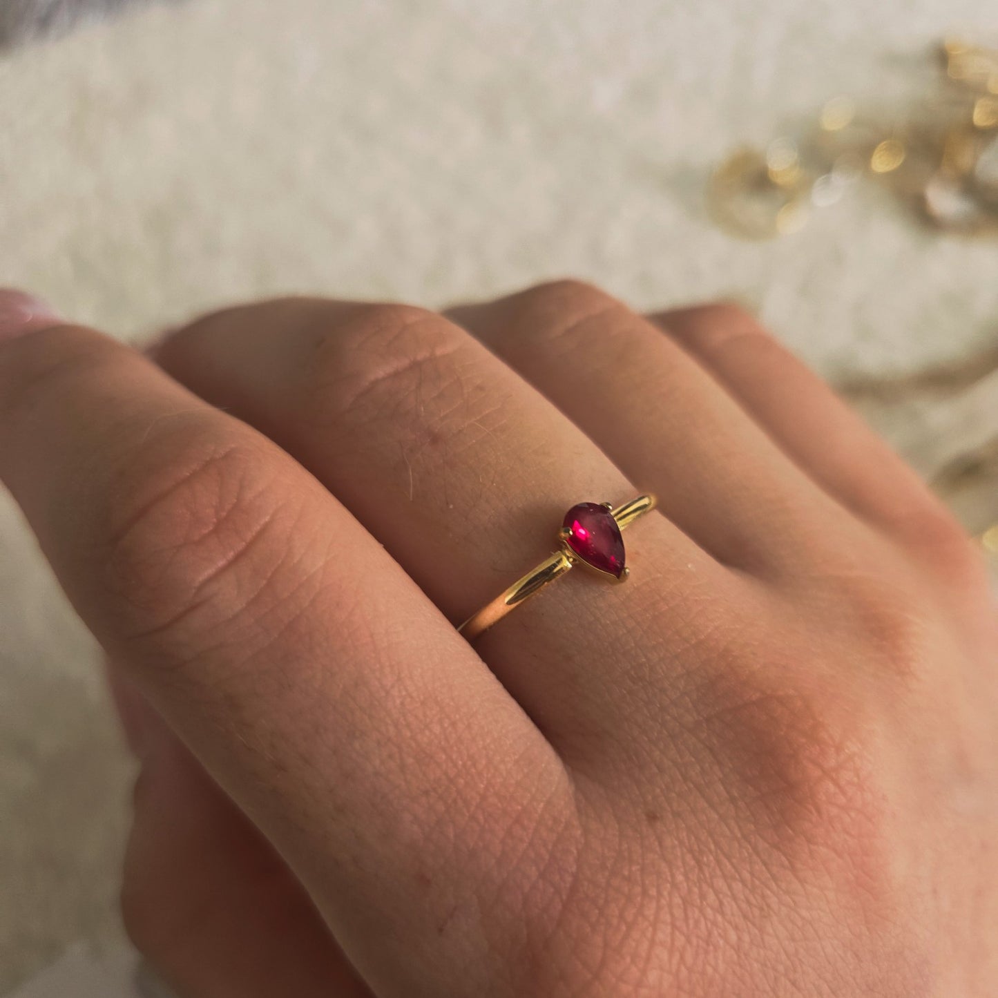 Bague dorée avec pierre rouge en forme de goutte portée à la main