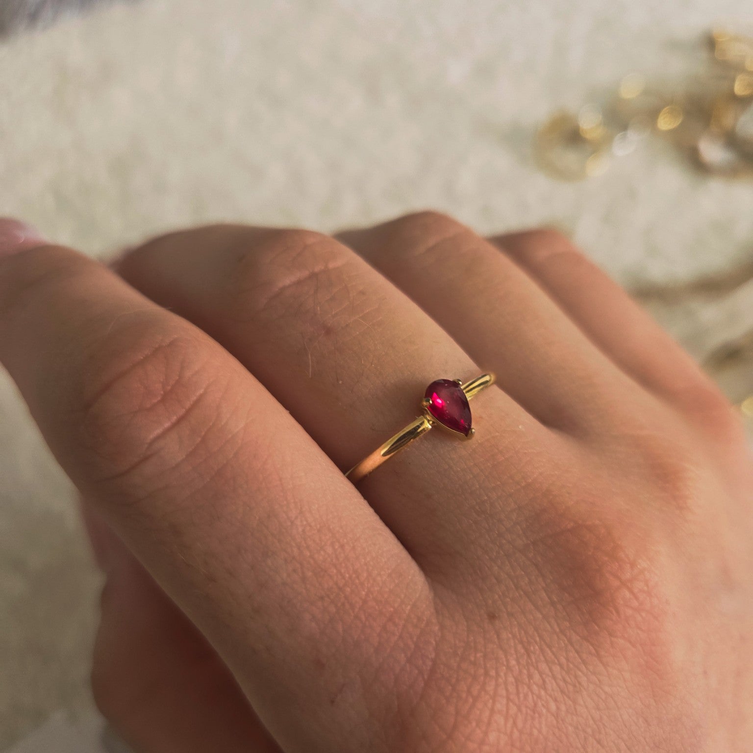 Bague dorée avec pierre rouge en forme de goutte portée à la main