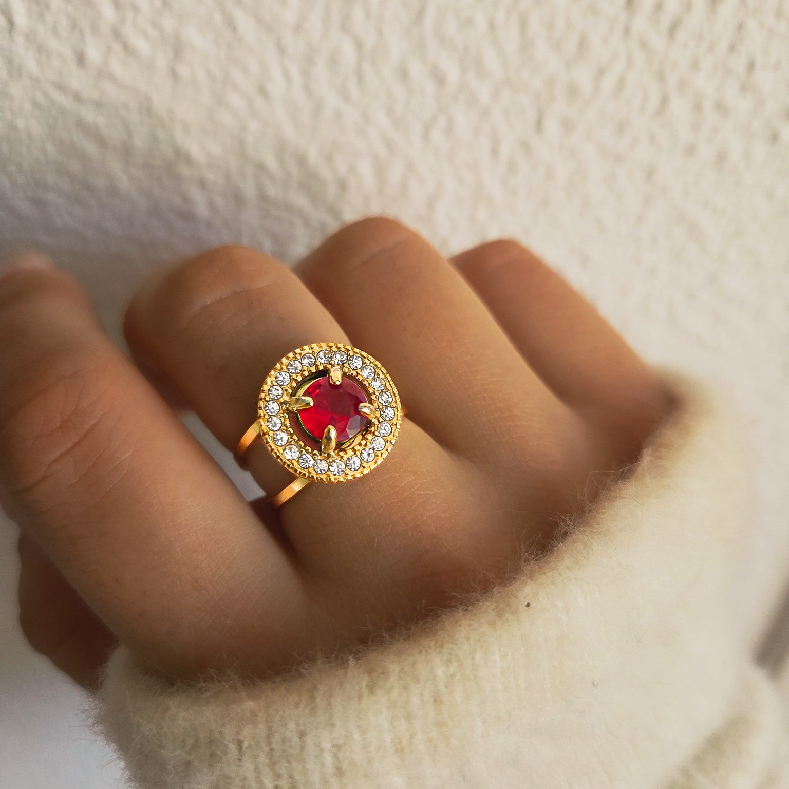 Bague dorée avec pierre rouge ronde entourée de strass portée à la main