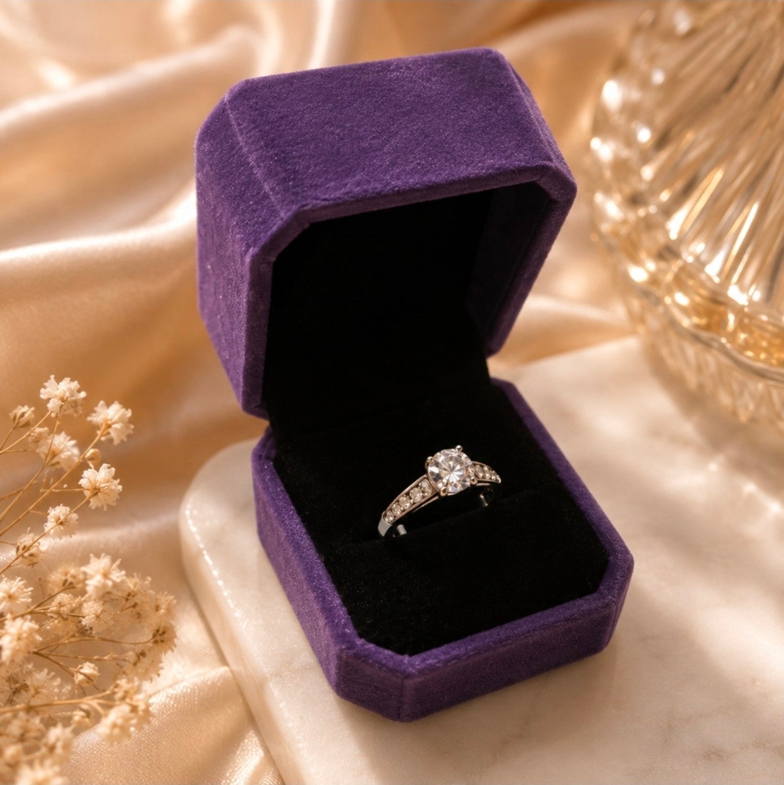 Bague solitaire argentée avec pierre centrale ronde et pierres blanches latérales présentée dans un écrin violet