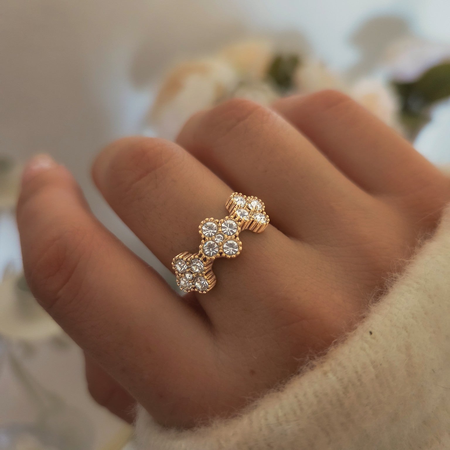 Bague dorée composée de trois fleurs pavées de strass portée à la main