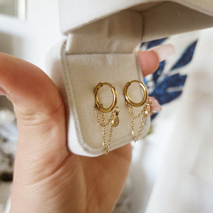 Boucles d'oreilles dorées avec chaînettes et pendentif goutte présentées dans un écrin