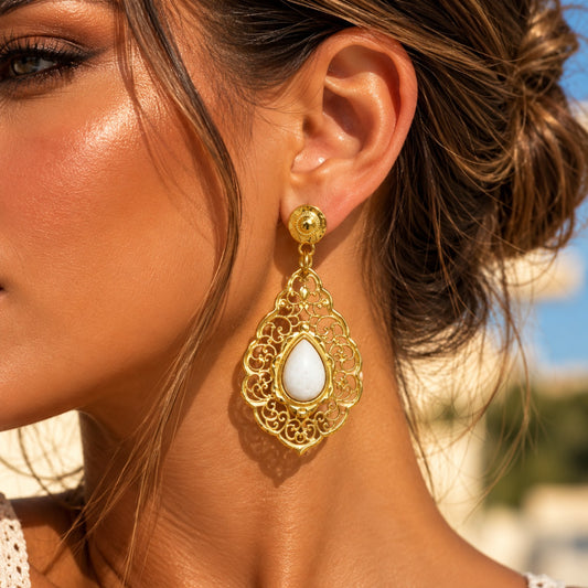 Boucle d’oreille pendante dorée à arabesques ajourées et cabochon blanc en forme de goutte
