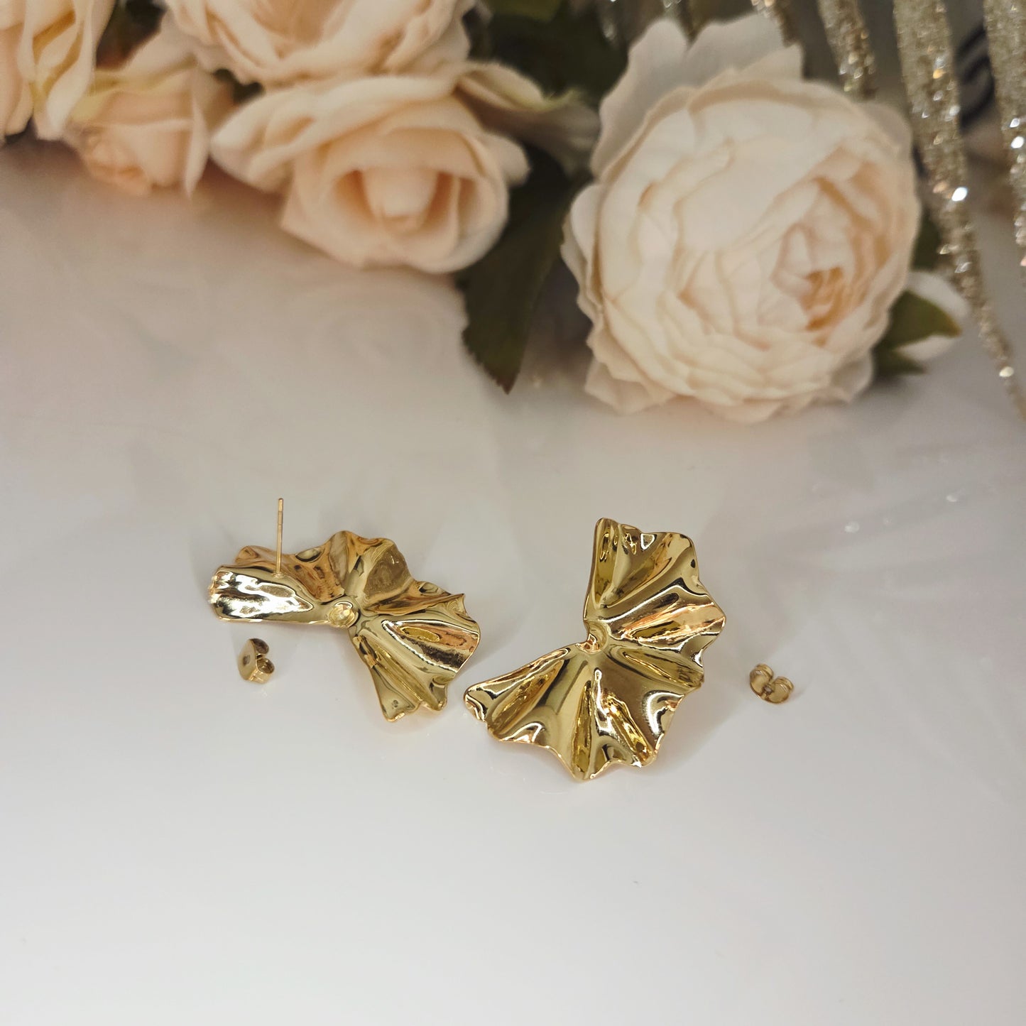 Boucles d’oreilles dorées sculptées posées sur fond clair mettant en valeur leur forme organique.