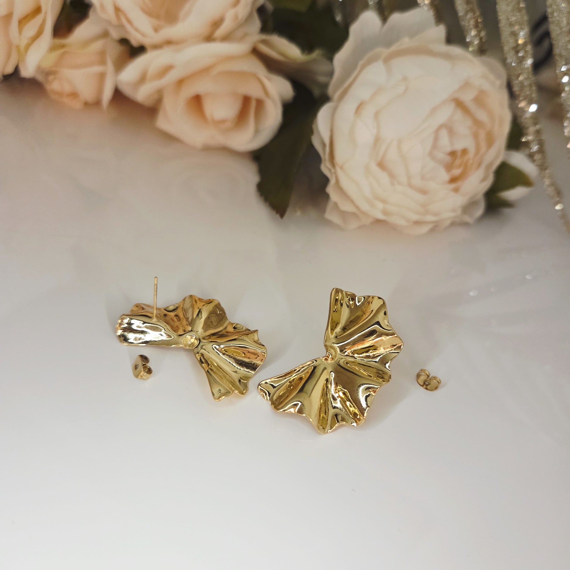 Boucles d’oreilles dorées sculptées posées sur fond clair mettant en valeur leur forme organique.