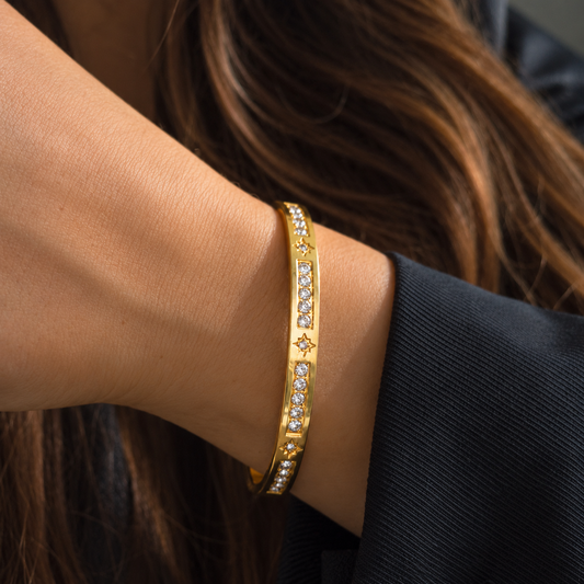 Bracelet jonc doré avec motifs étoiles et rangées de petites pierres transparentes, porté au poignet