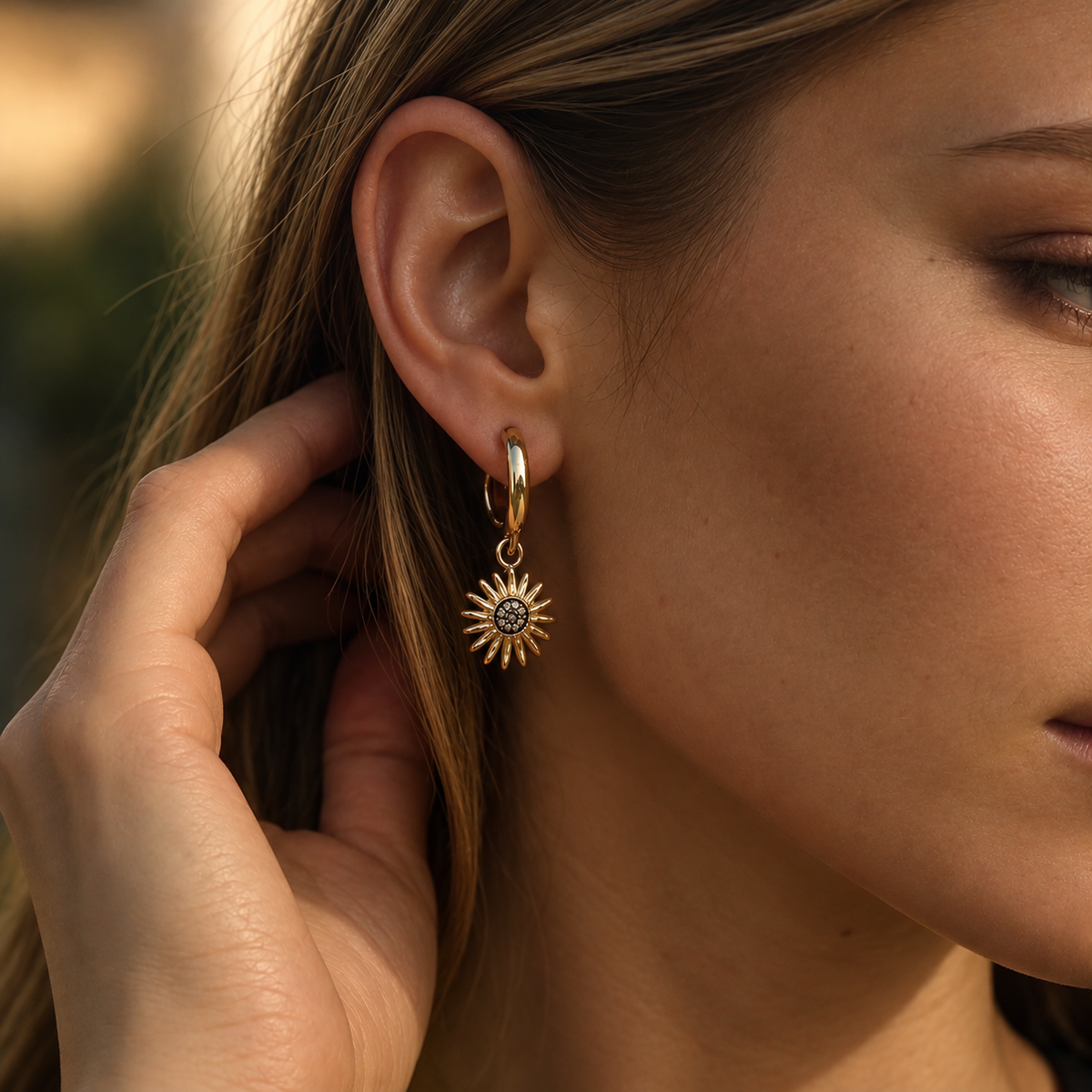 Boucle d’oreille créole dorée à pendentif soleil avec centre sombre orné de petites pierres scintillantes